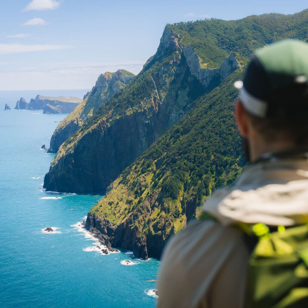 A hiker stands overlooking green cliffs leading into the ocean.