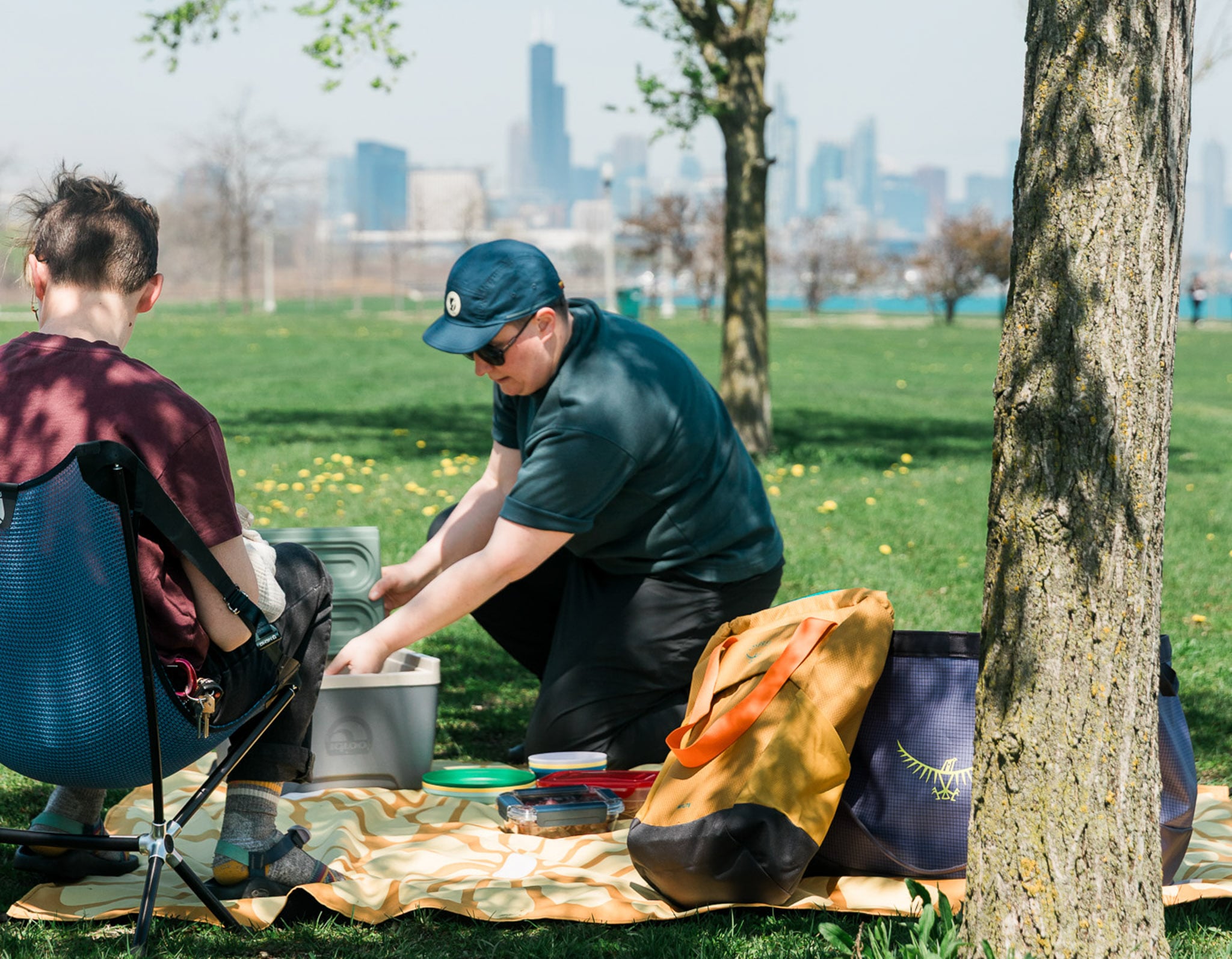 Two people enjoy a picnic in a park with the Chicago skyline as a backdrop.