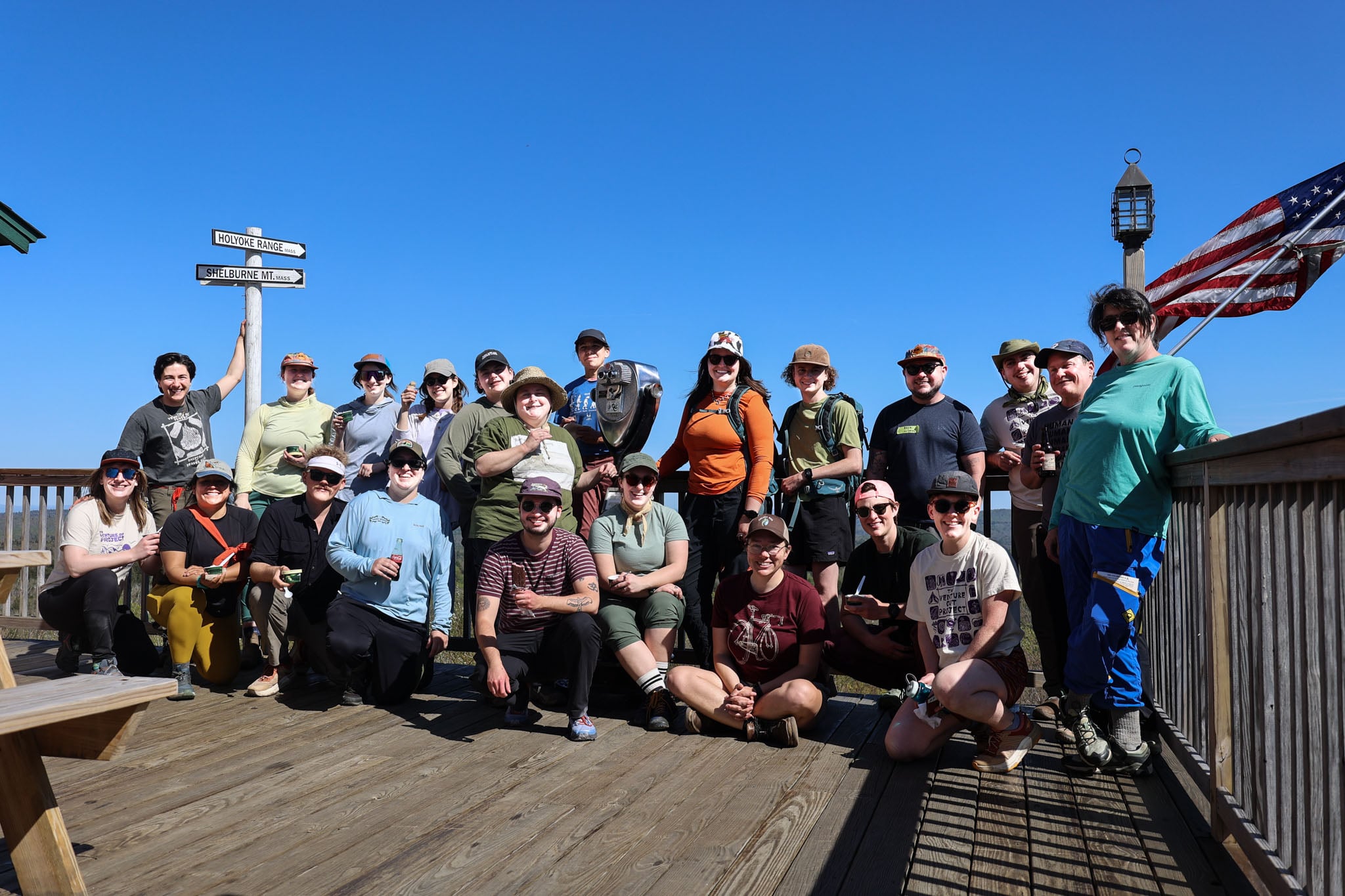 A group of people pose on a wooden deck under the blue sky.