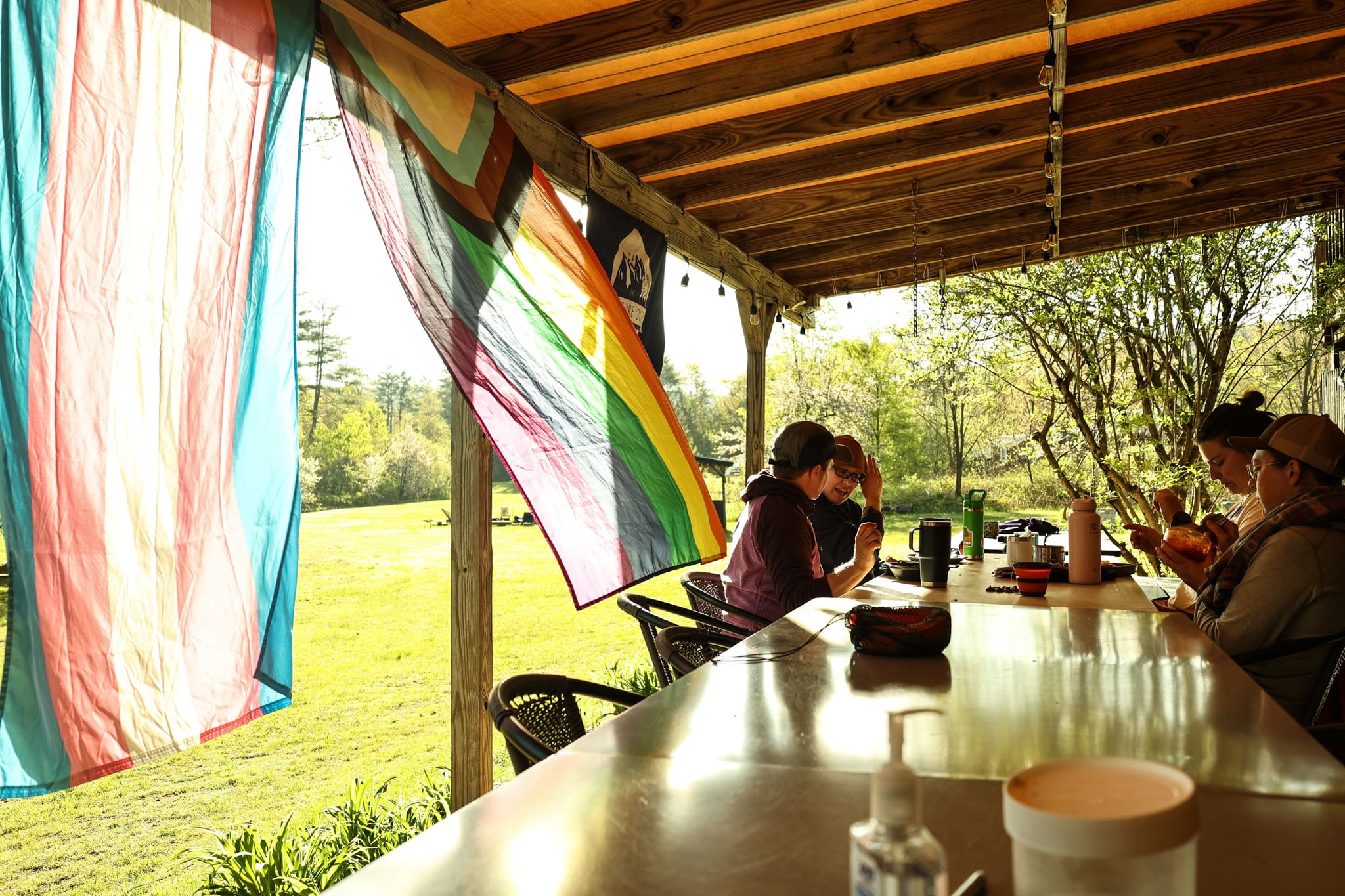 Four people sit at a table under a porch roof, flags waving in the wind.
