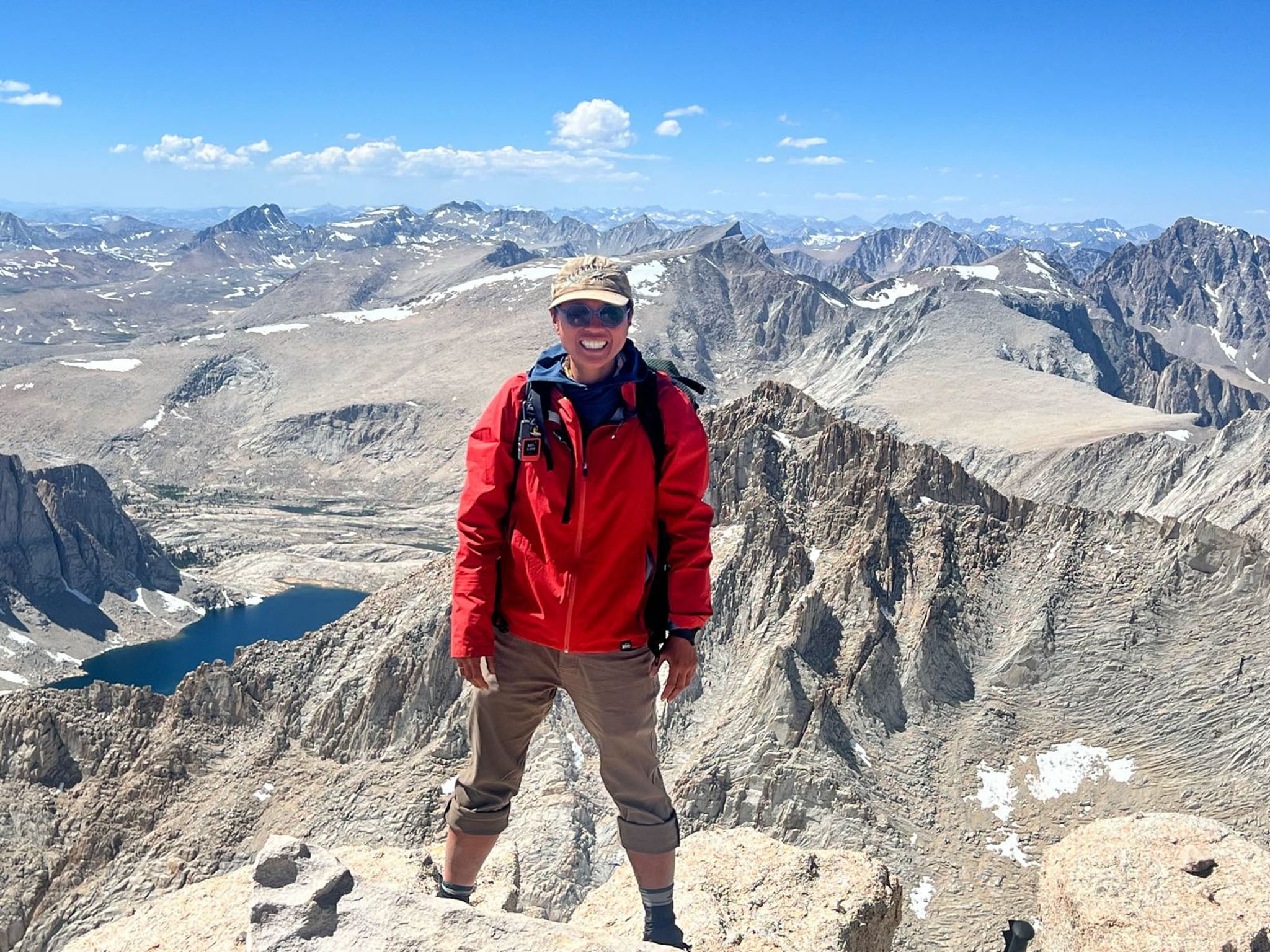 A person stands at the top of a mountain with an expanse of other mountains in the background.