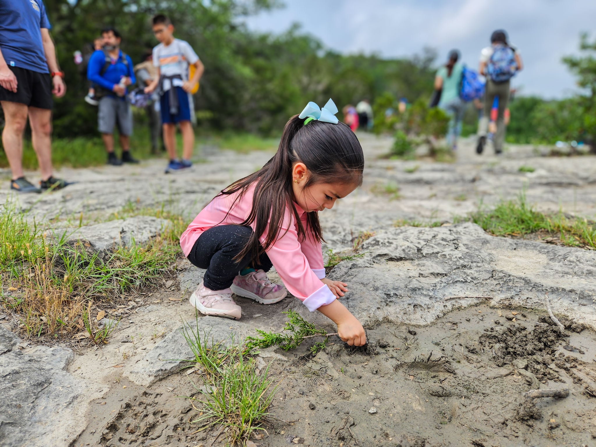 A child crouches down on a rock and draws in the mud with a stick.