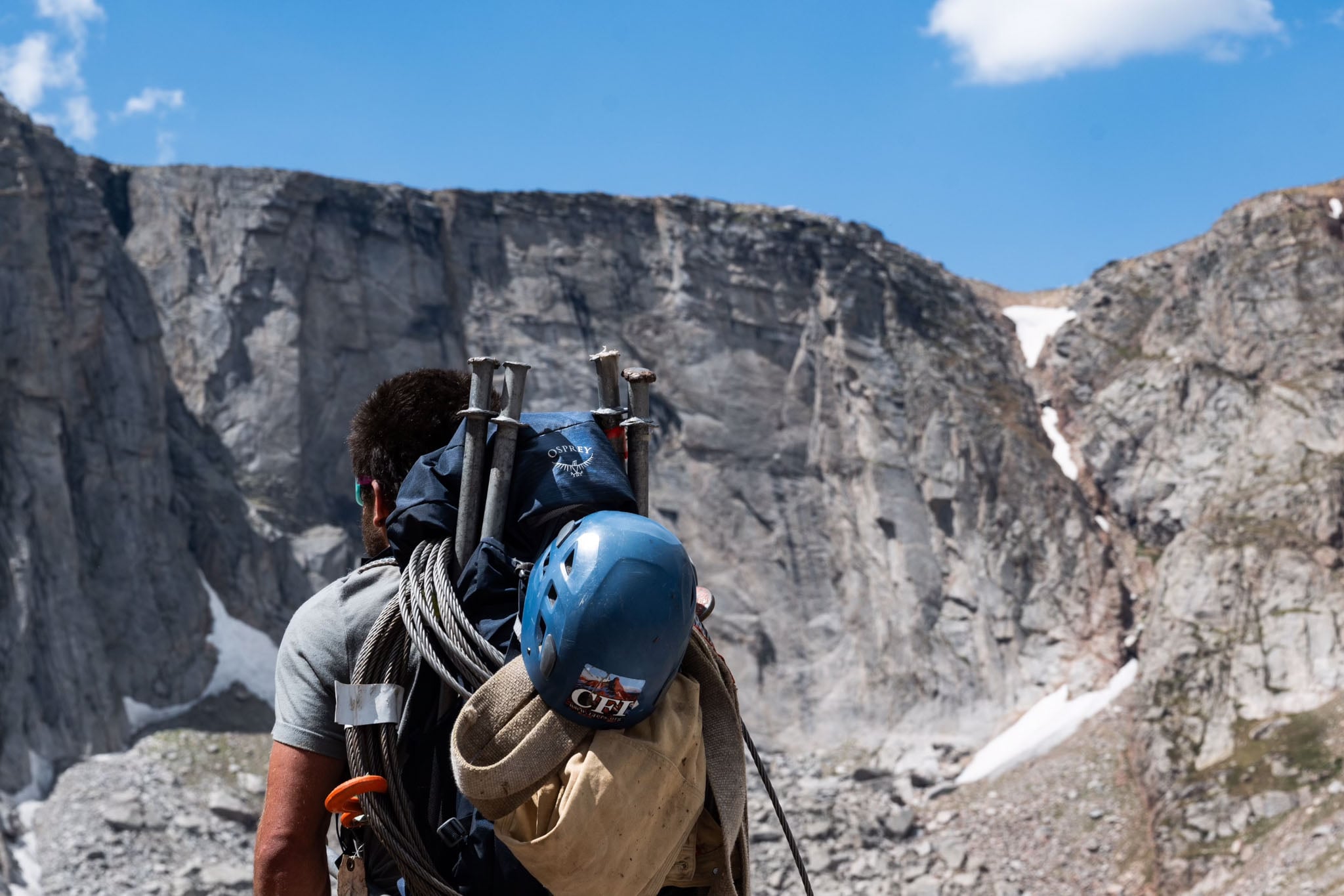 A person stands on a rocky setting with their pack loaded with gear.