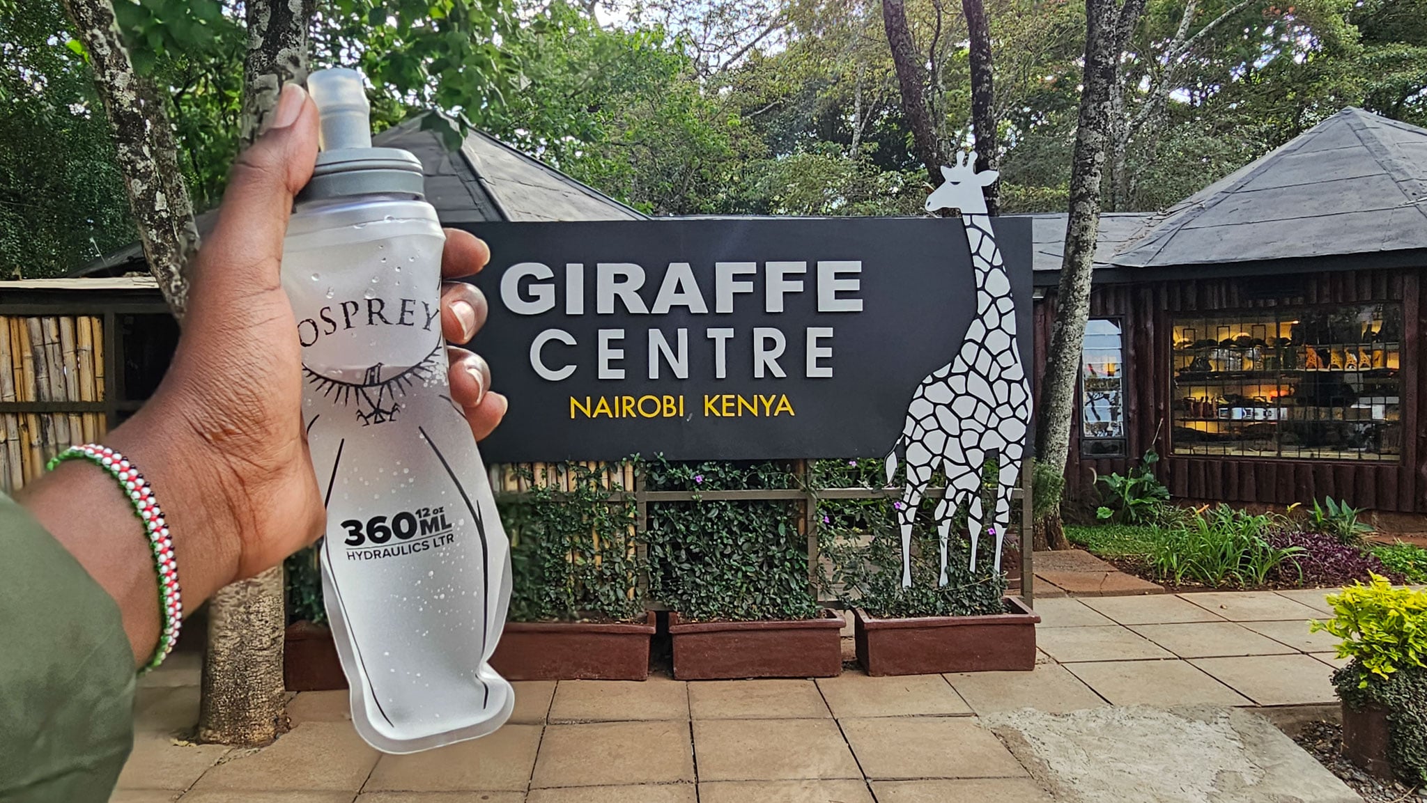 A water bottle held up in front of a sign for a giraffe center.