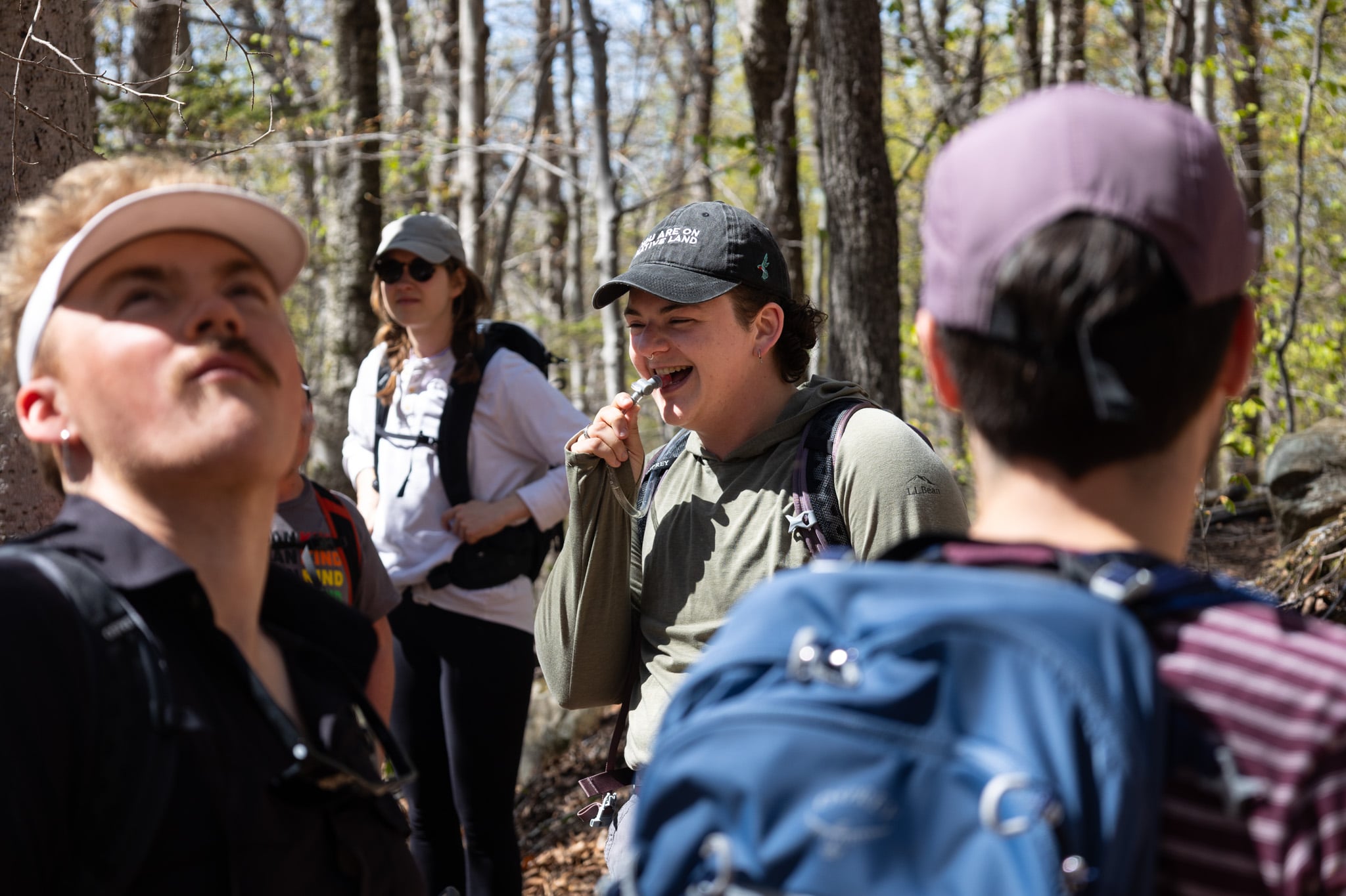 A group of people stand in the woods raising their hands and smiling.