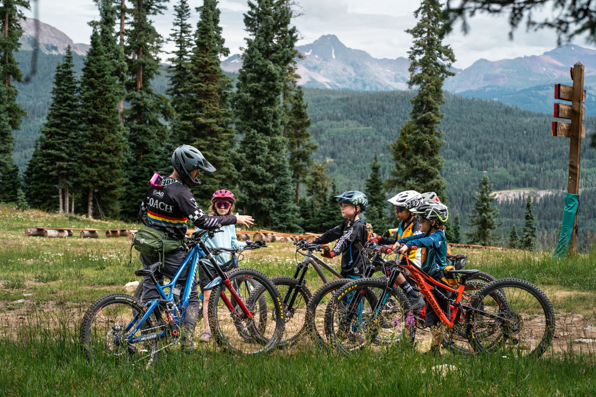 A coach talks to a group of kids with bicycles and helmets.