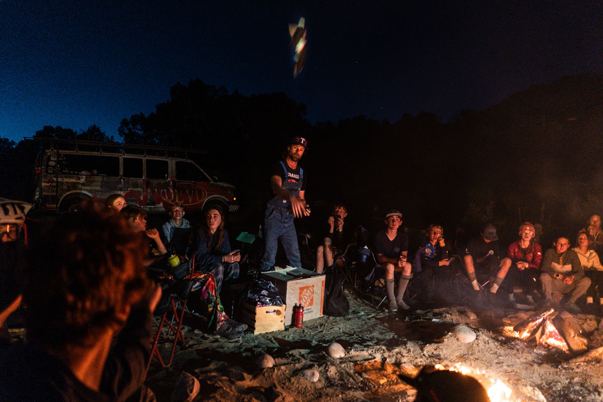 A person stands amidst a group of kids around a campfire next to a Durango Devo van.