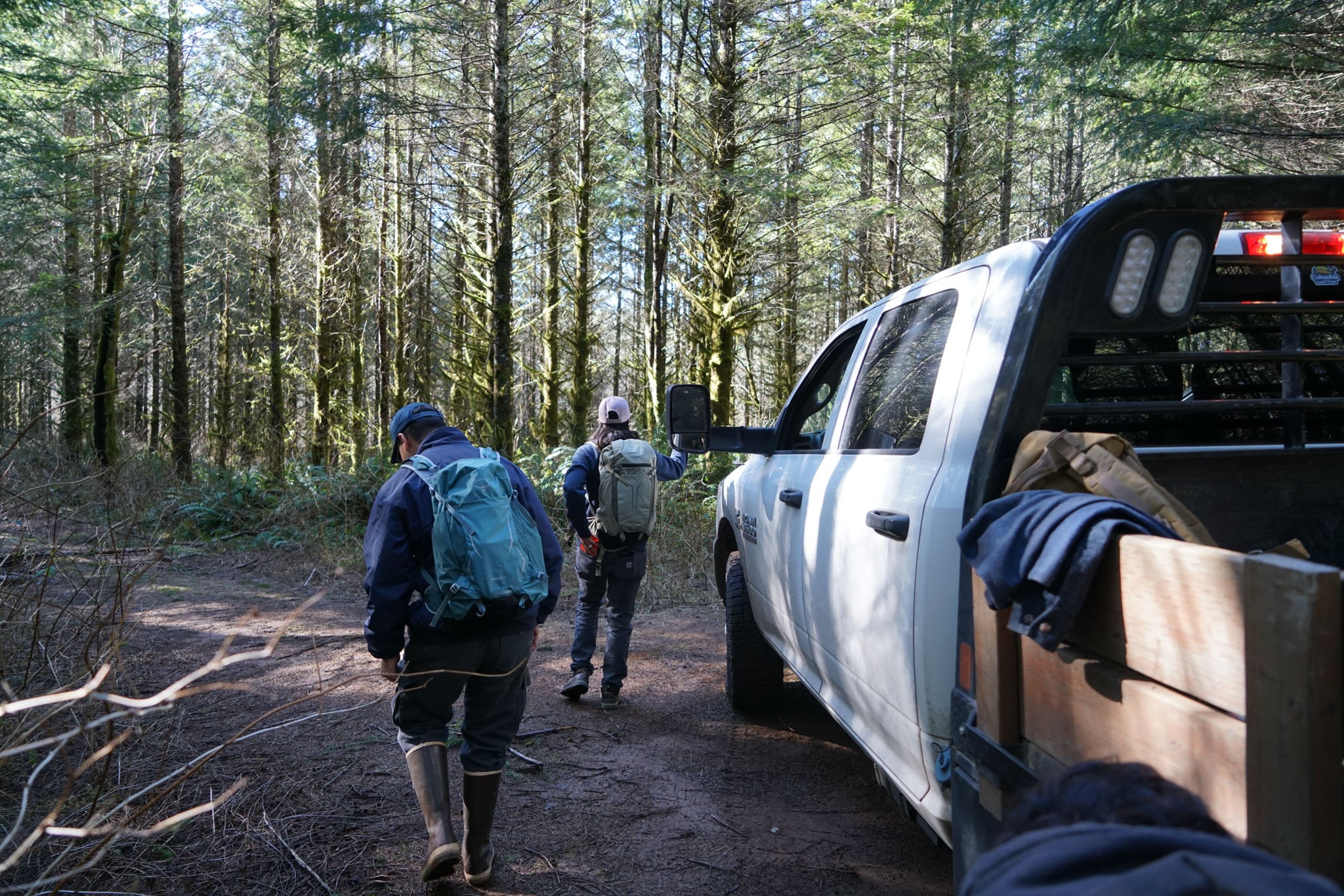 Two people embark on a trail from their work truck.
