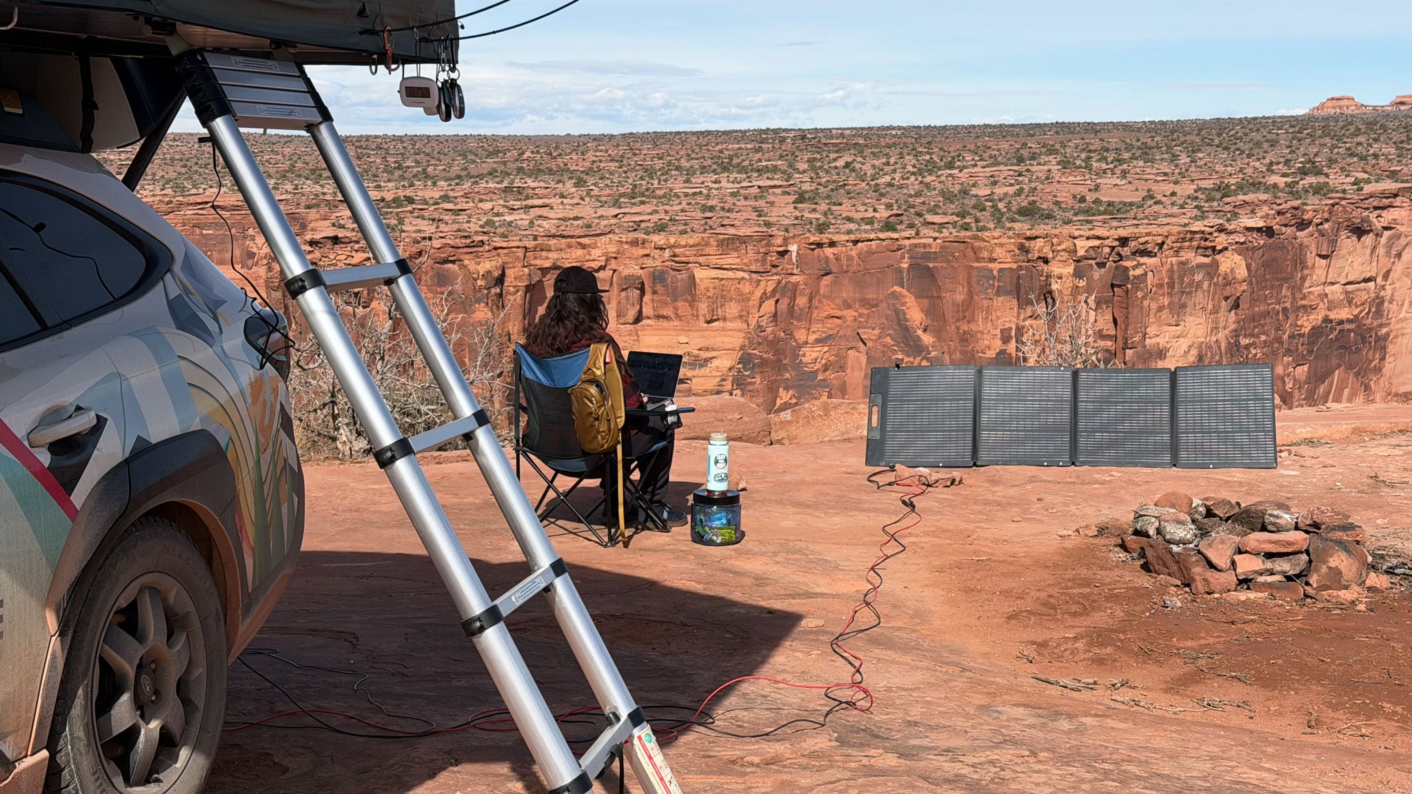 A person sits in a chair overlooking a rocky canyon on their computer.