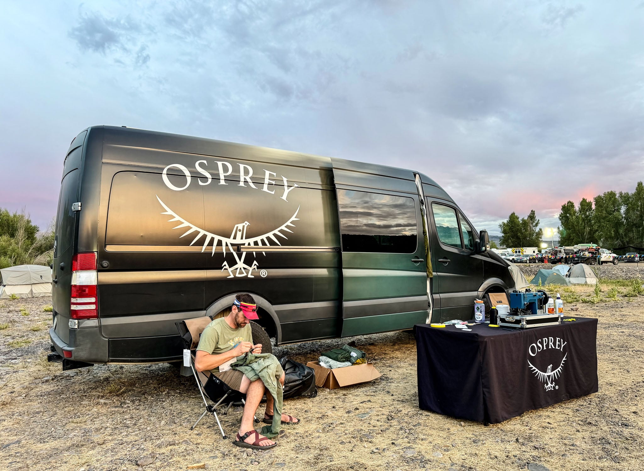 A person sits in front of the Osprey van next to a sewing machine repairing items.