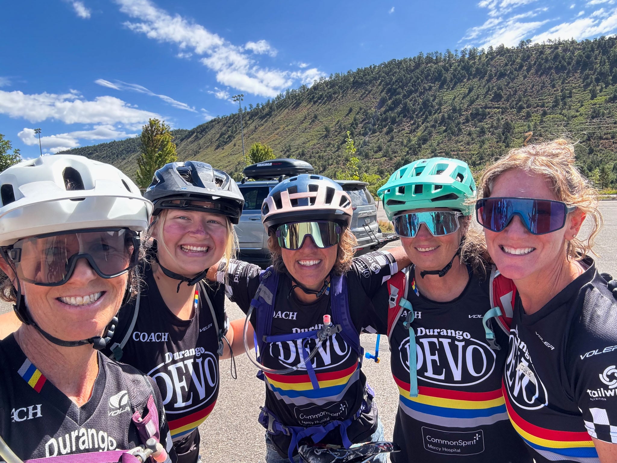 Five cyclists wearing jerseys and backpacks pose for the camera.