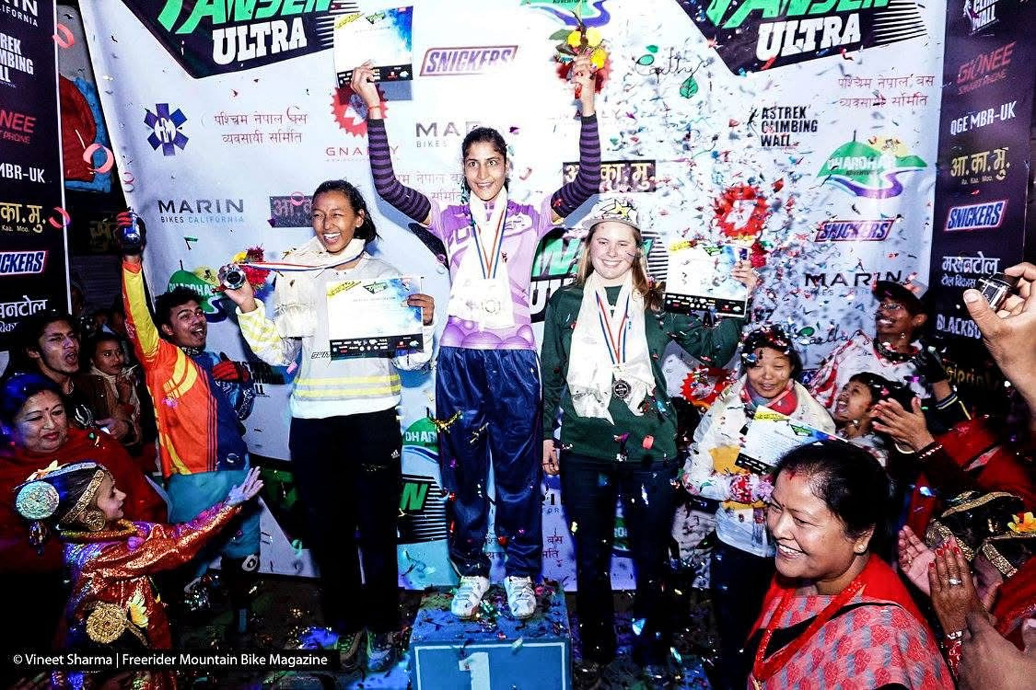 Three people stand on a podium, celebrating.