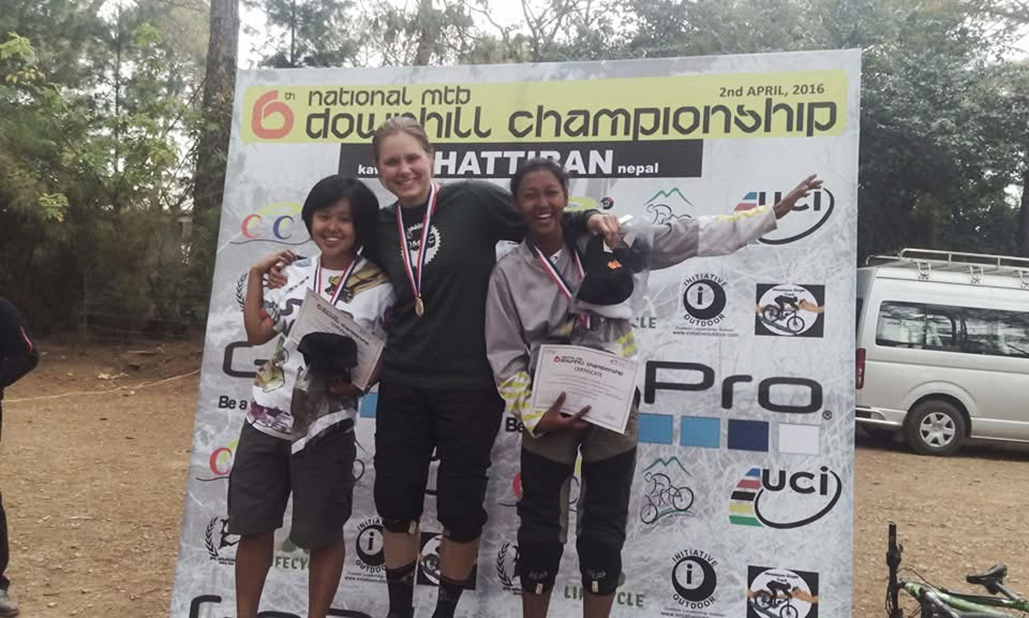 Three people stand on a podium showing off their certificates and medals.