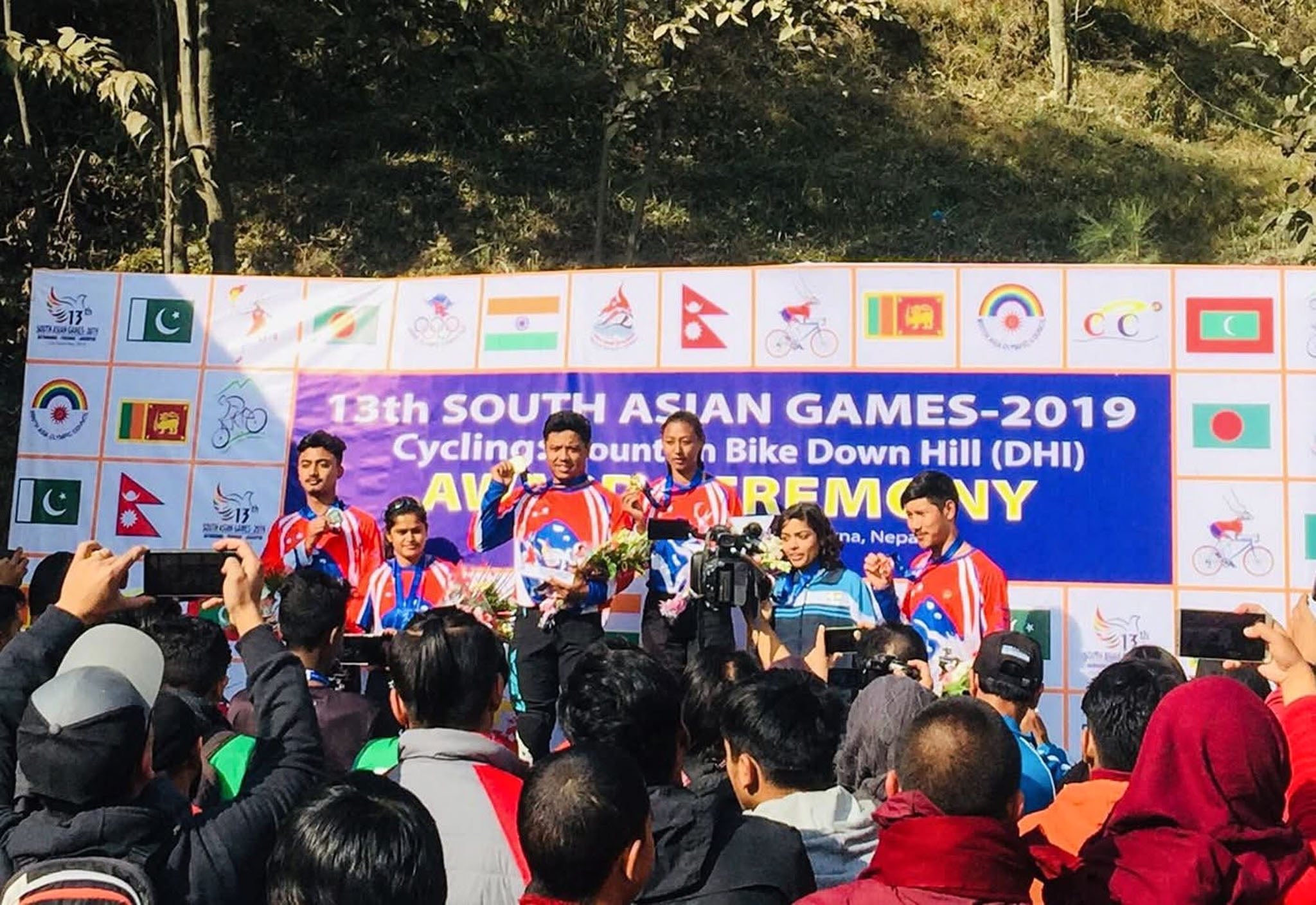 Six people stand at a podium showing off their medals.