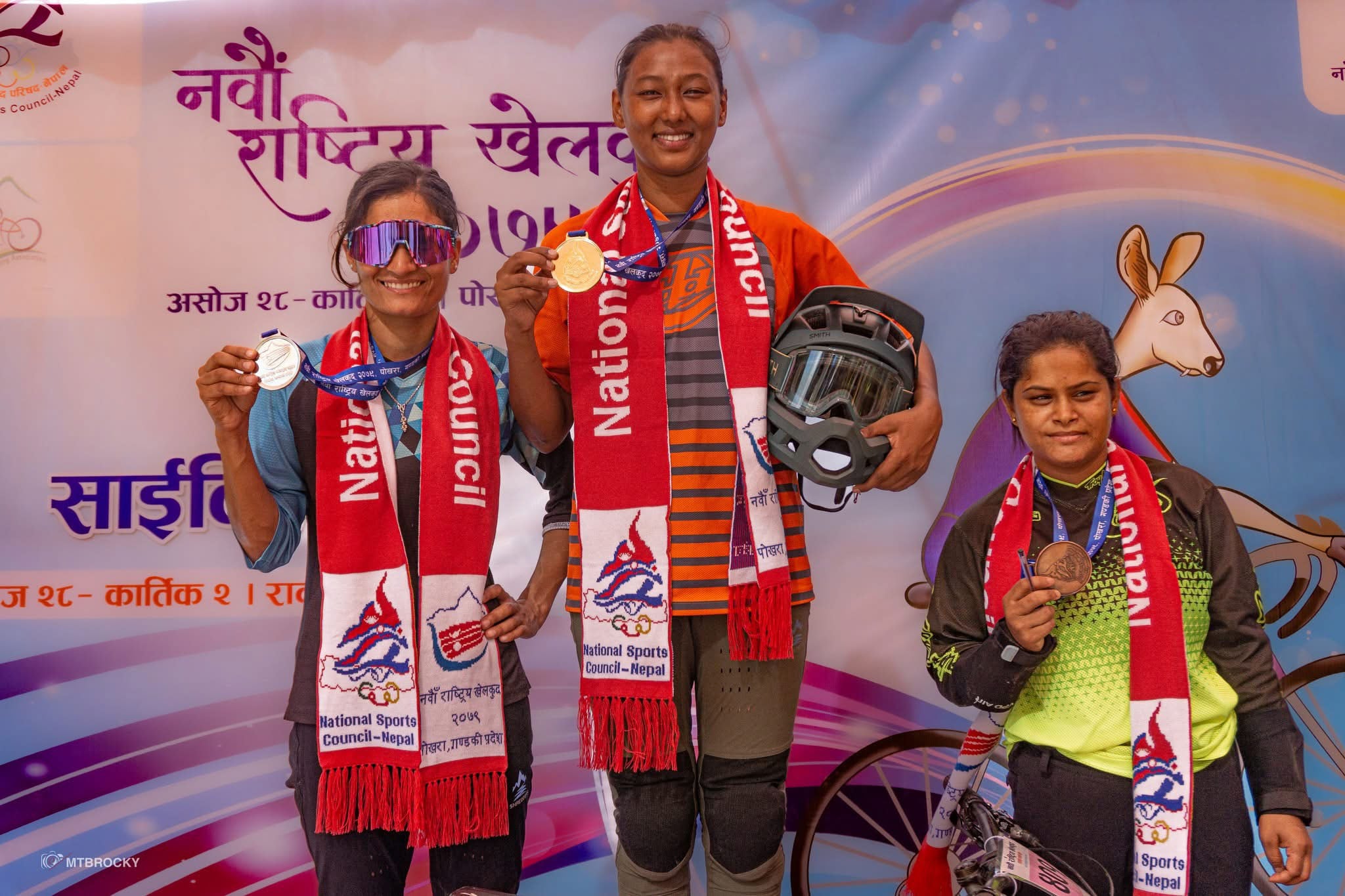 Three people hold their medals up on the podium smiling.