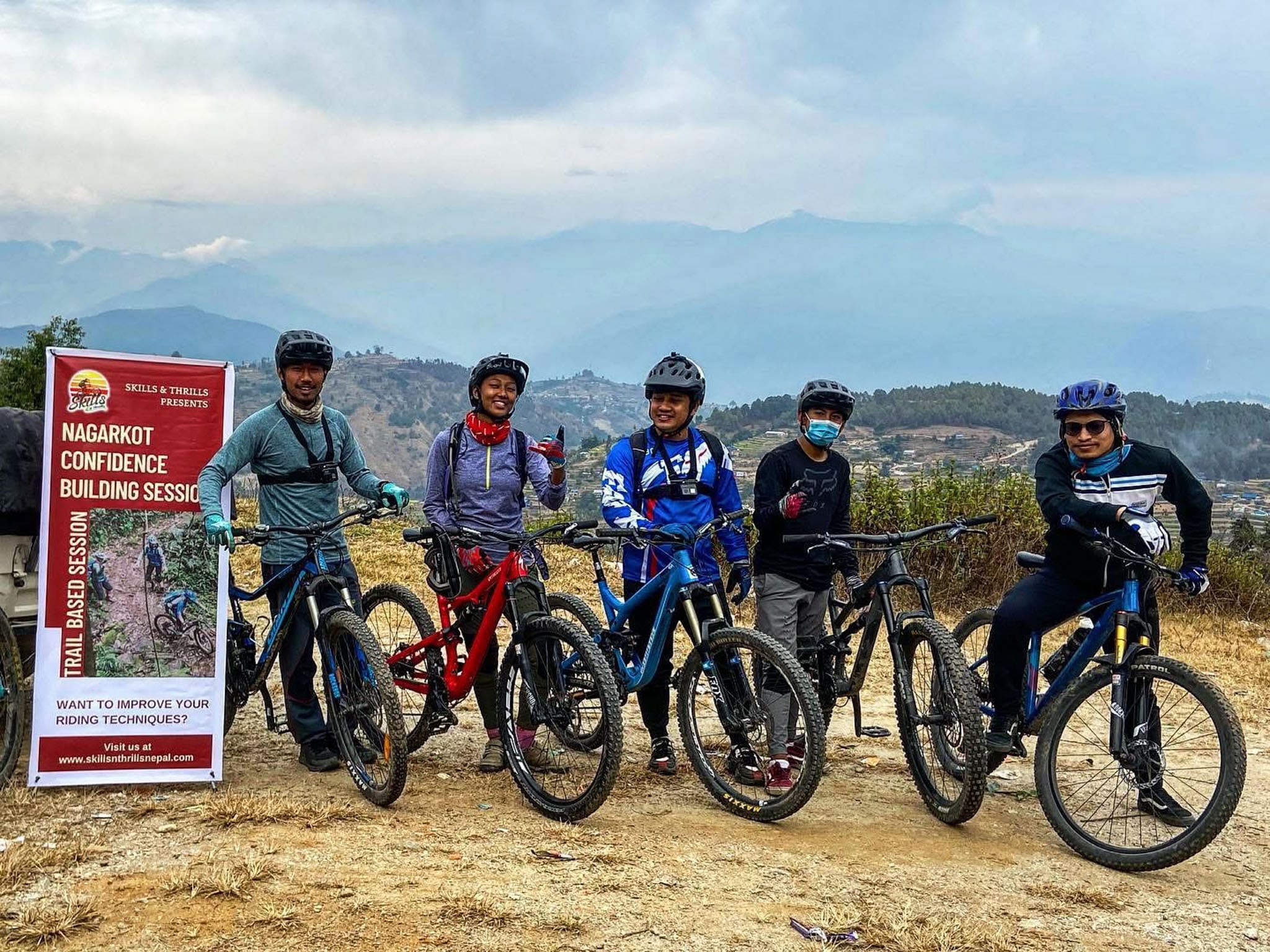 Five people pose with their bikes next to a banner.