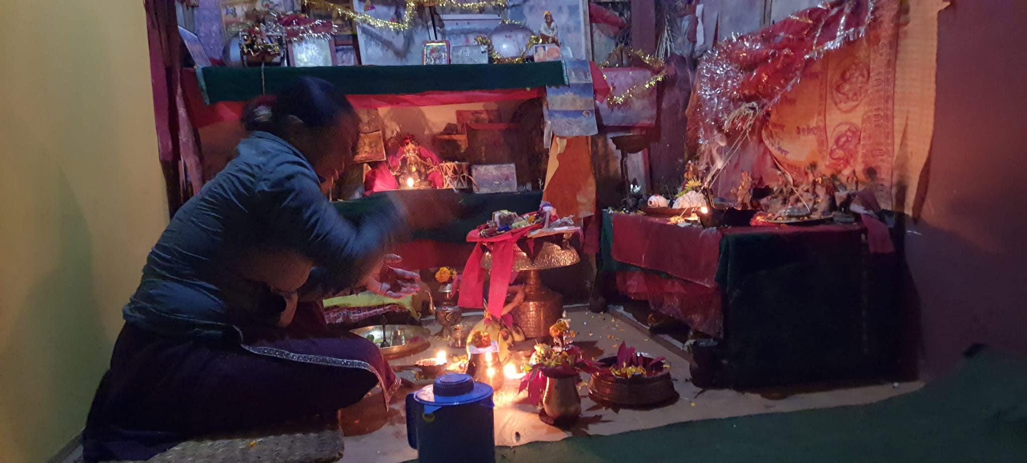 A person prays at a shrine lit by candles.