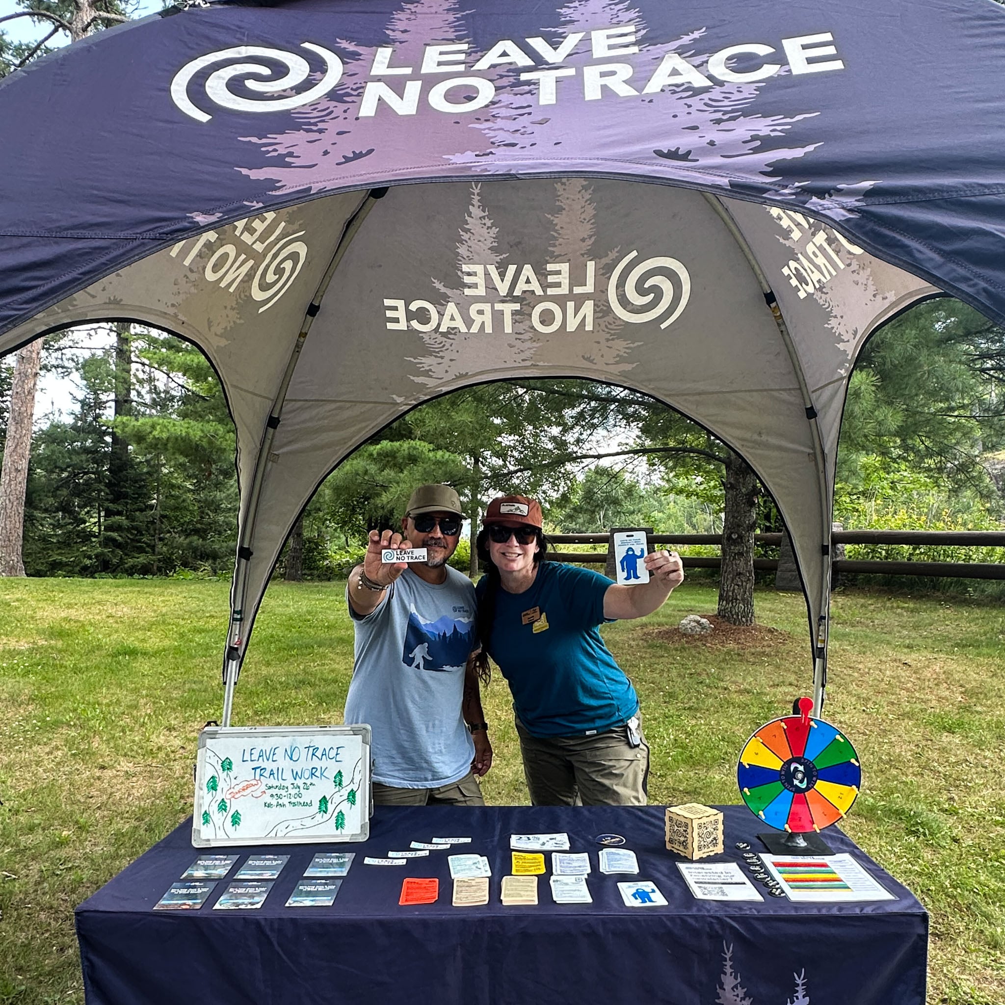 Two people stand behind a table under a Leave No Trace Tent.