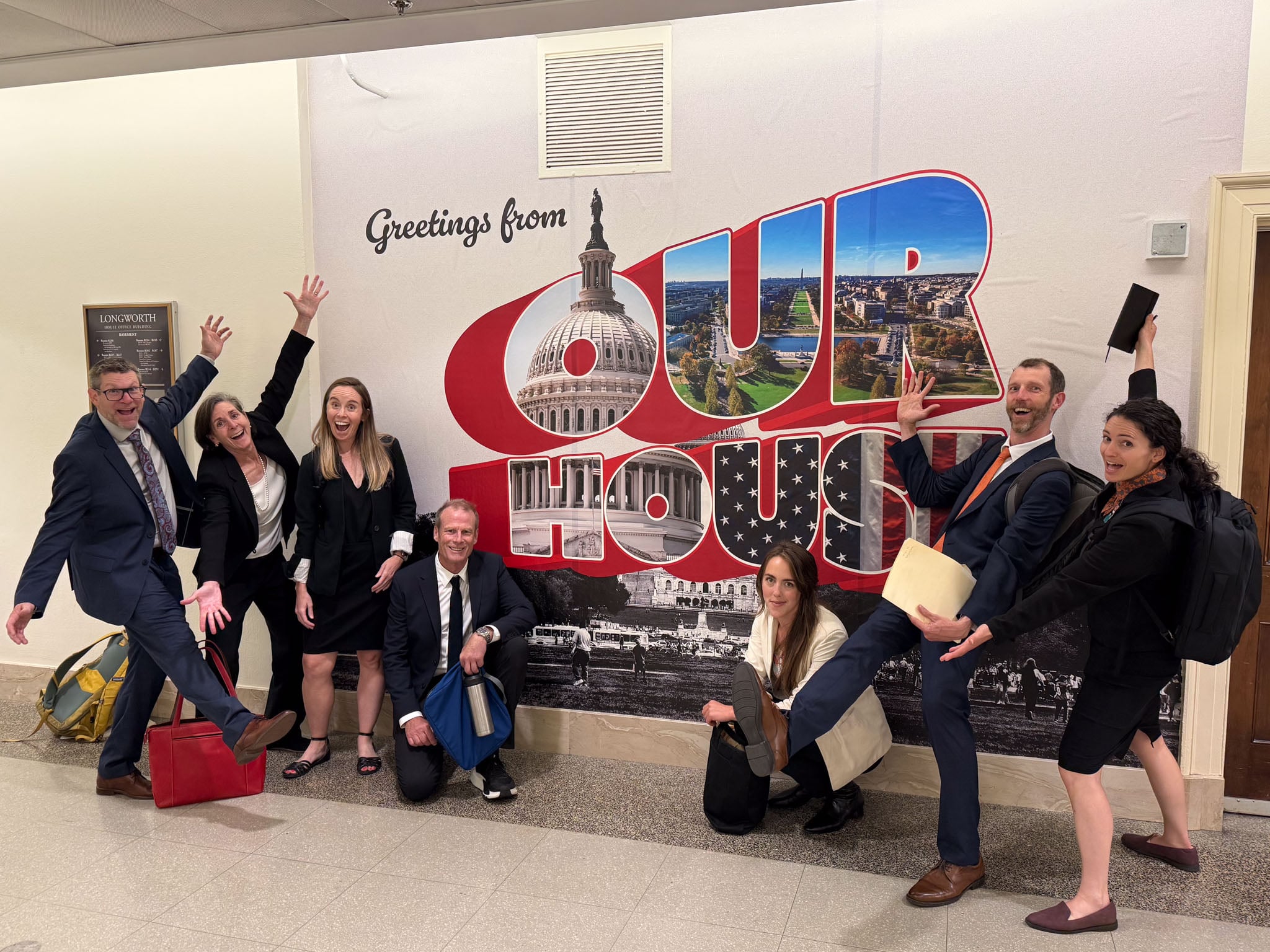 A group of people pose in front of a mural that says Our House.