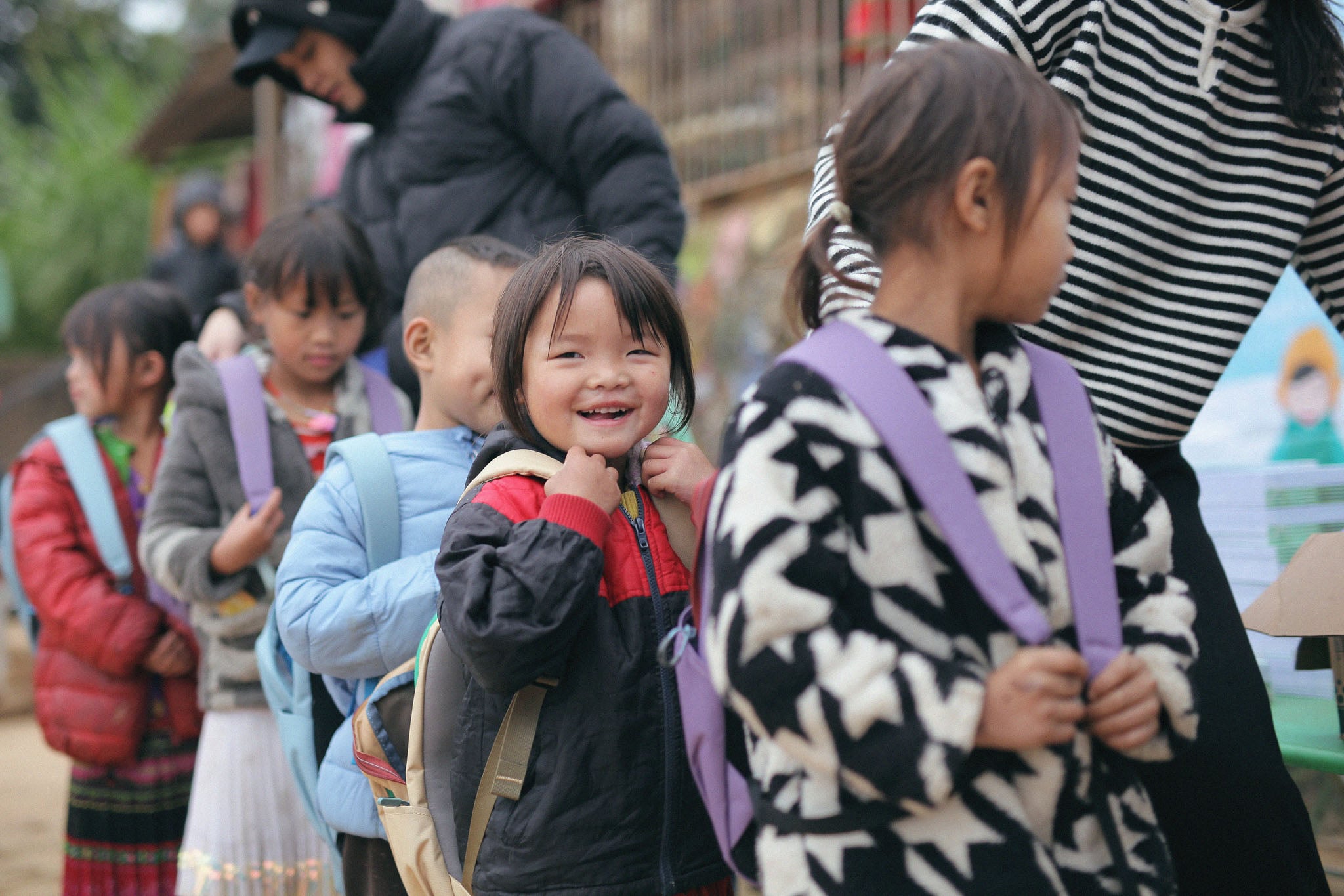 Kids line up wearing backpacks, one child smiles at the camera.