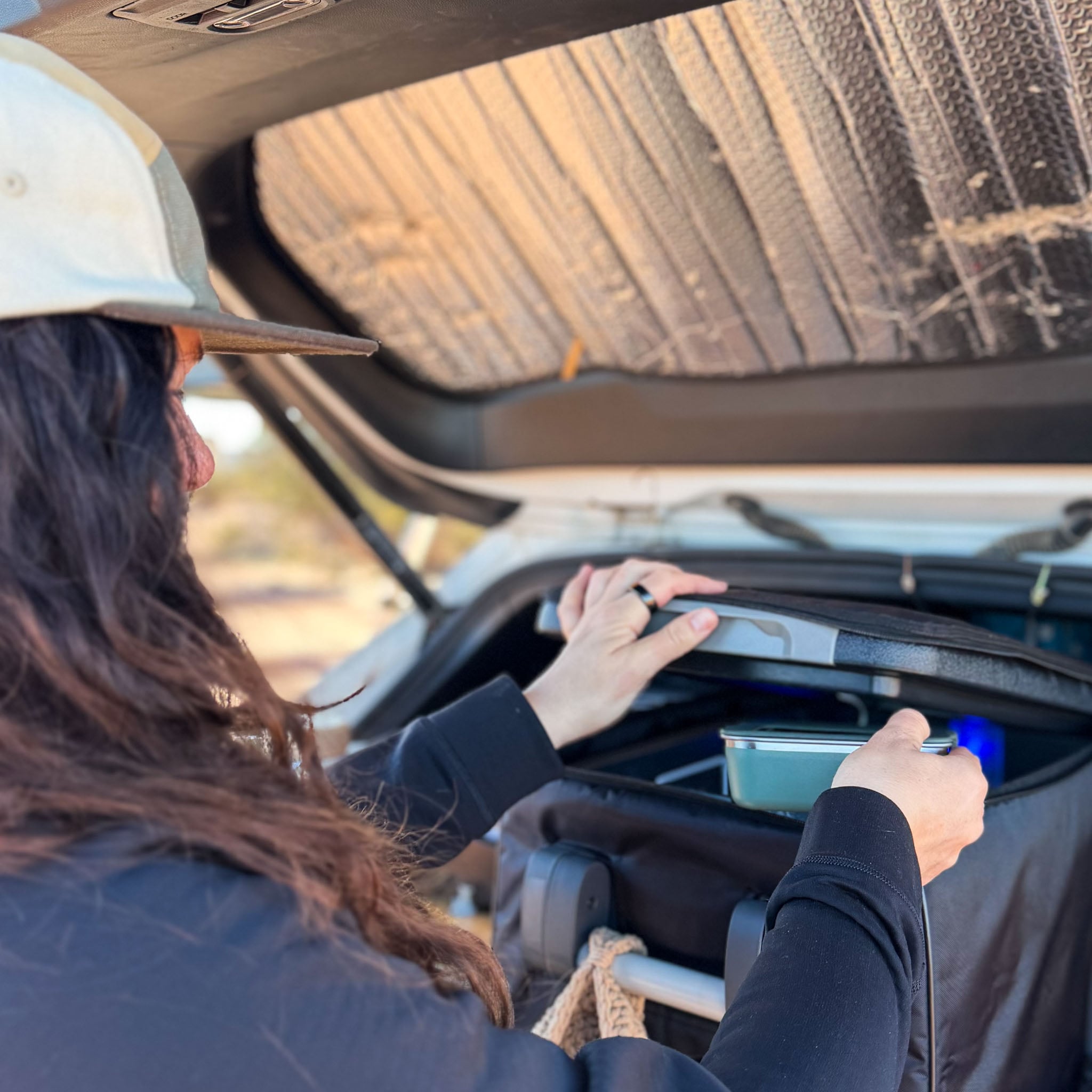 A person lifts a reusable container out of a cooler in the trunk of a car.