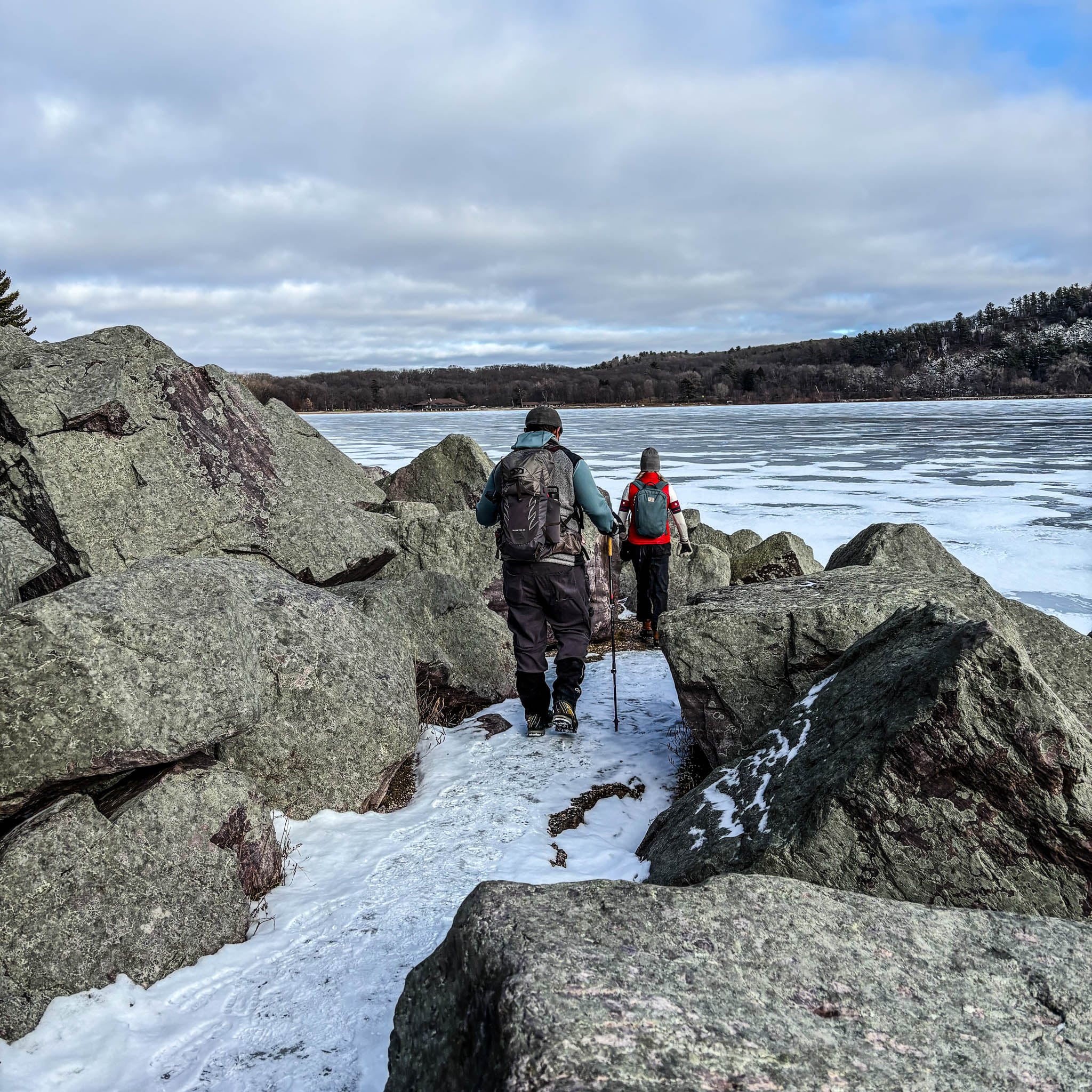 Two people walk along a lakeside path over a light dusting of snow.