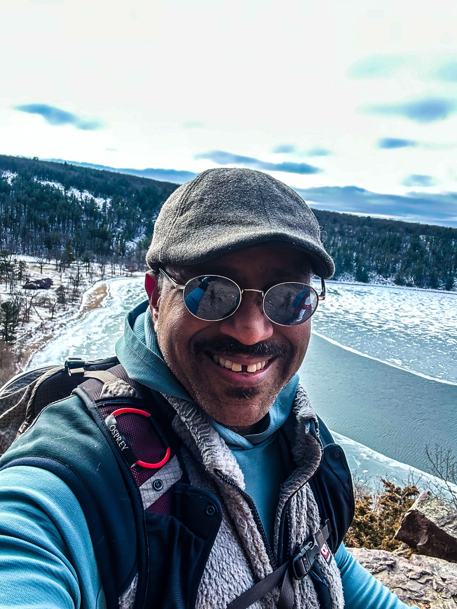 A man takes a selfie while on a walk in the winter, partially frozen lake in the background.