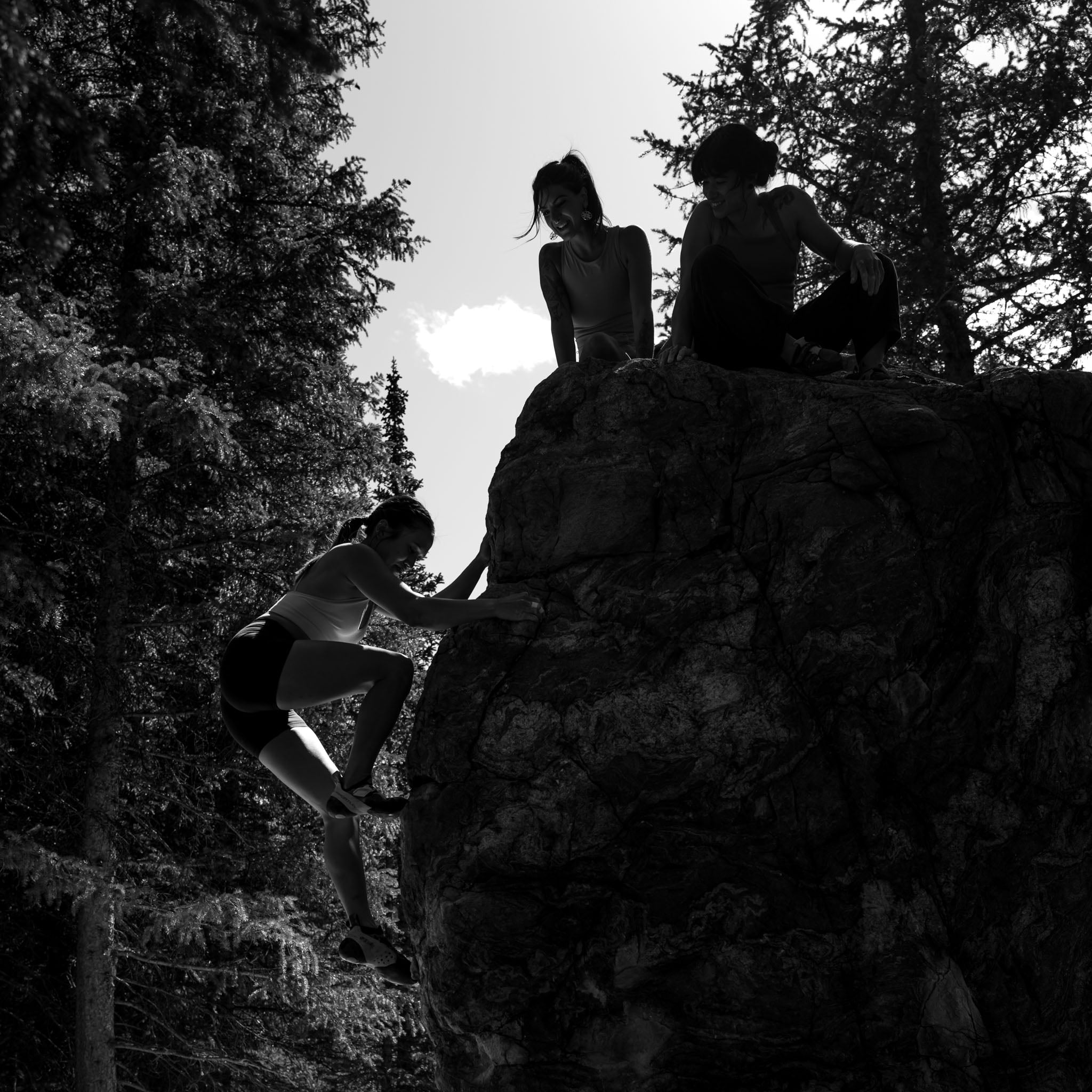 One person climbs a boulder, two people sit on top.