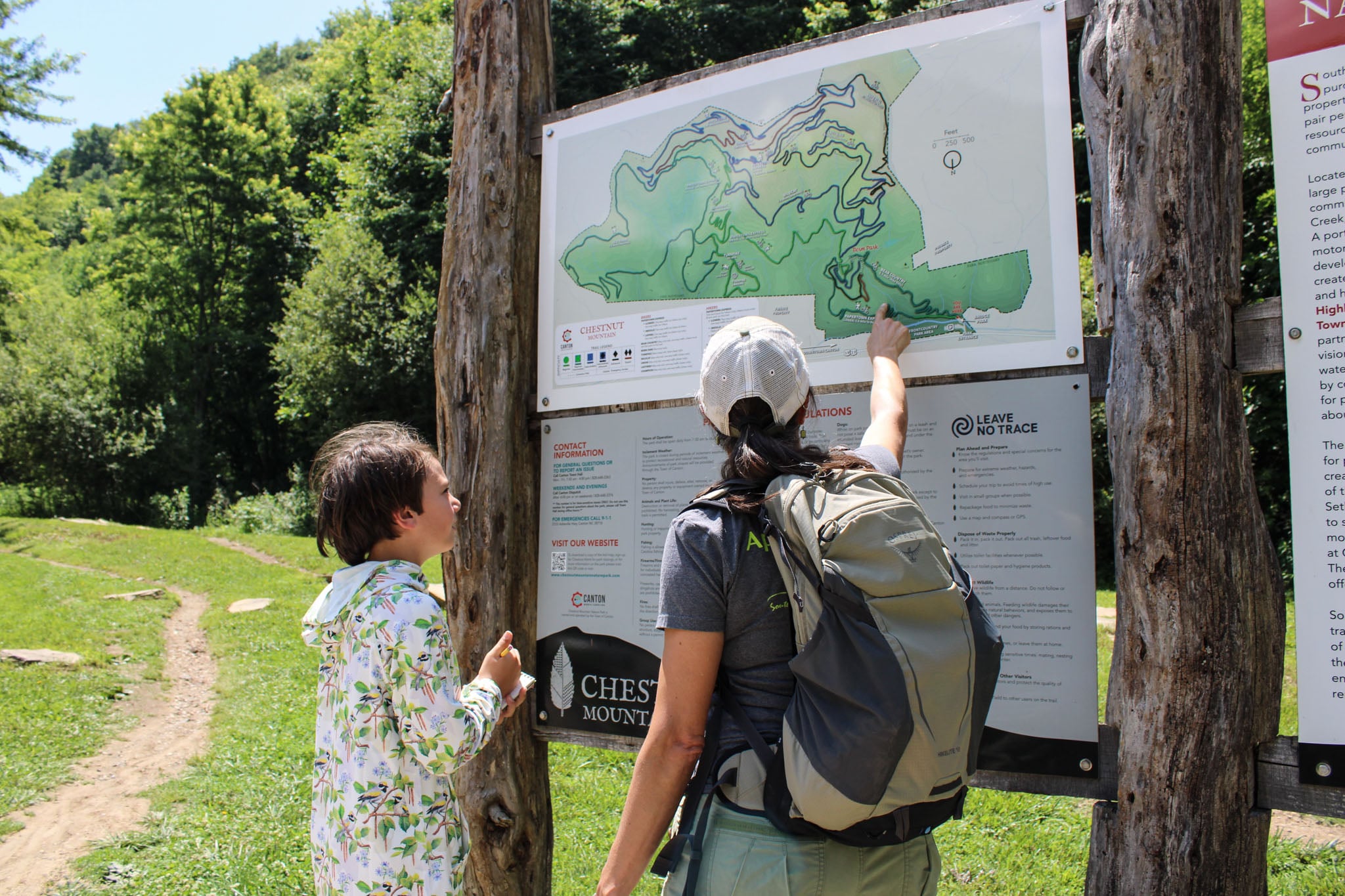Two people map out their route on posted signage at a trailhead.