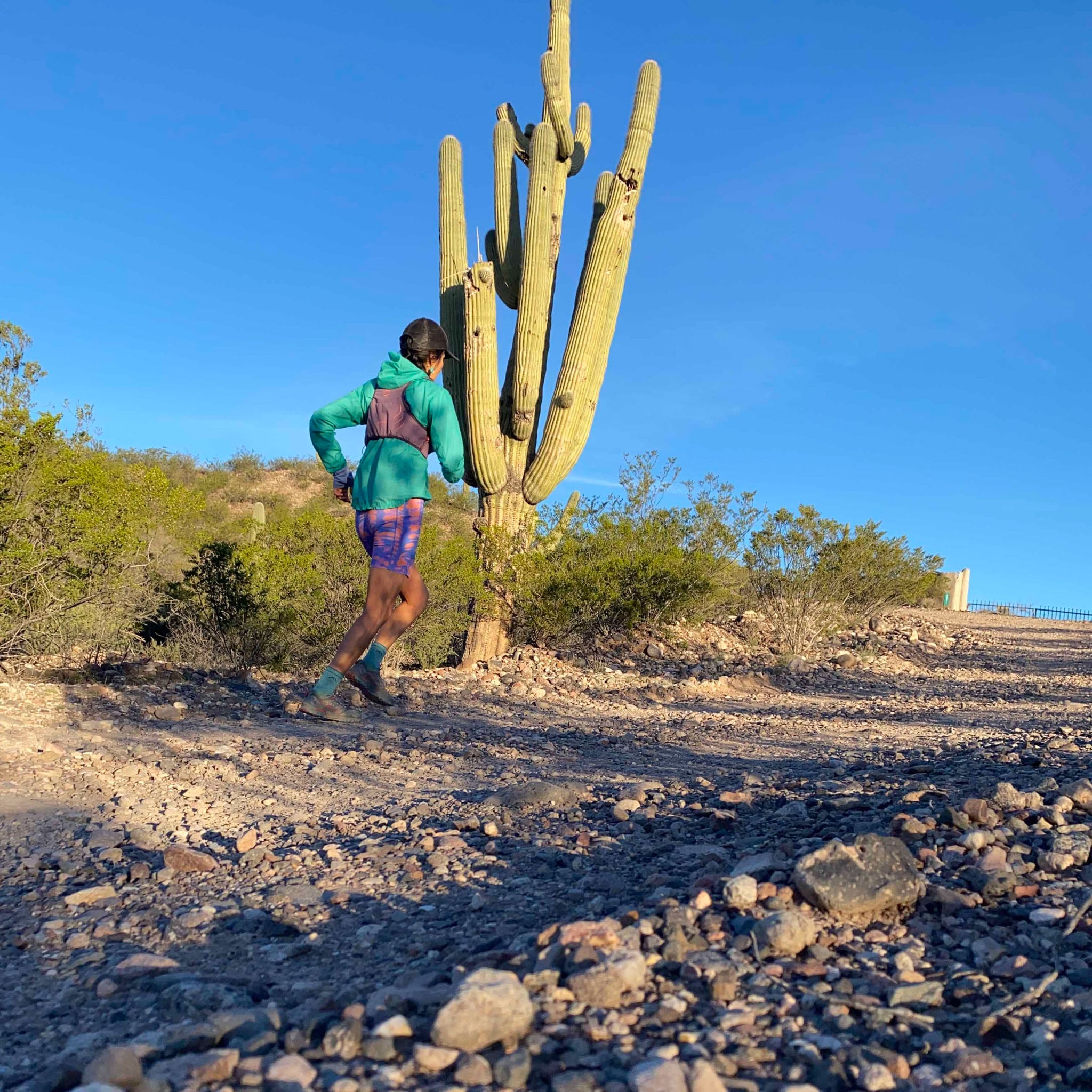 A person runs on a trail past a saguaro cactus.