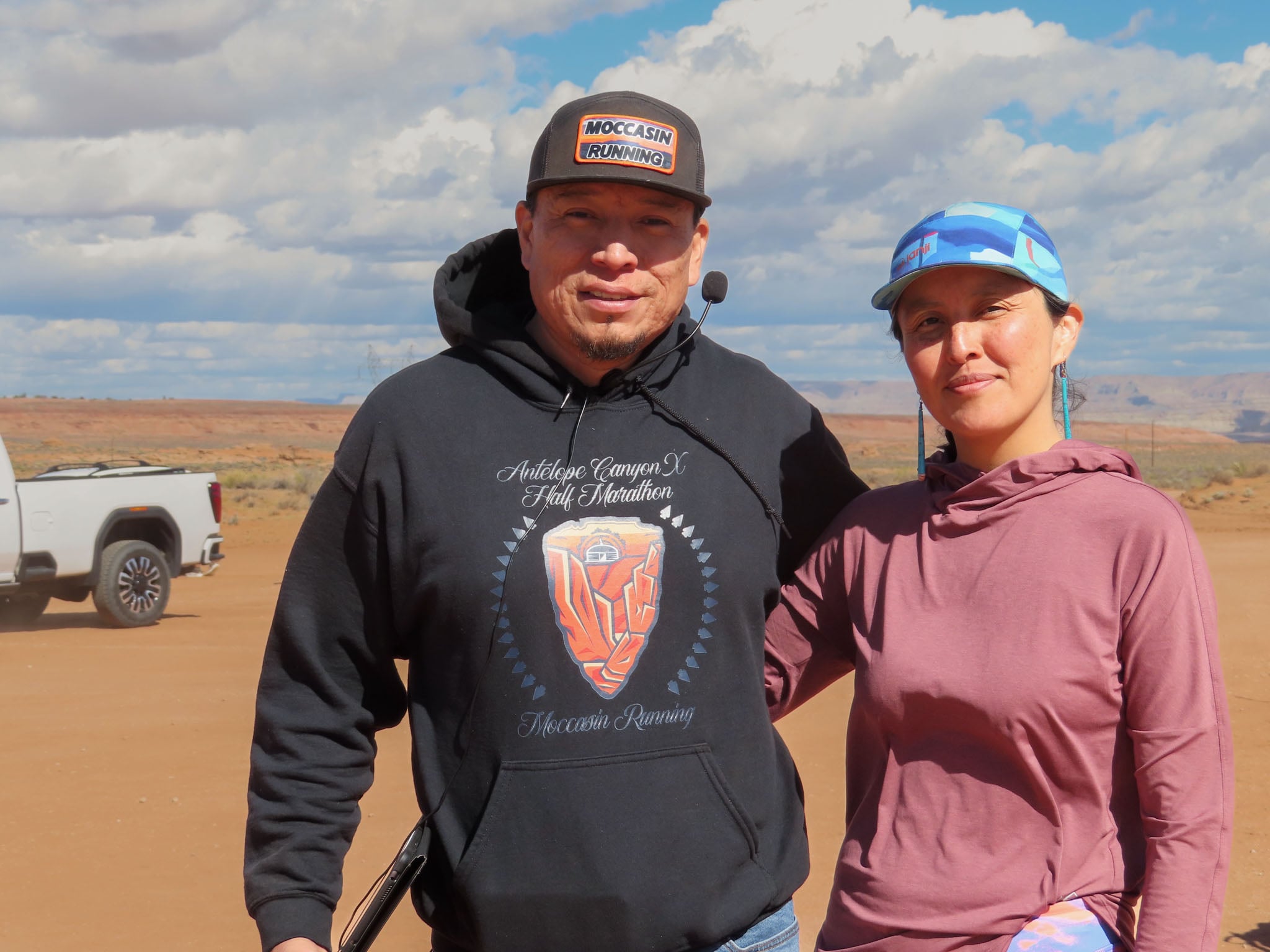 Two people pose in front of the camera, the desert and blue sky in the background.
