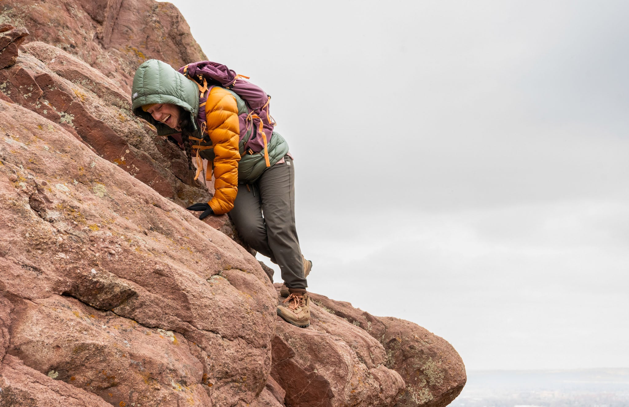 A person scrambles over rocks in a light snow flurry.