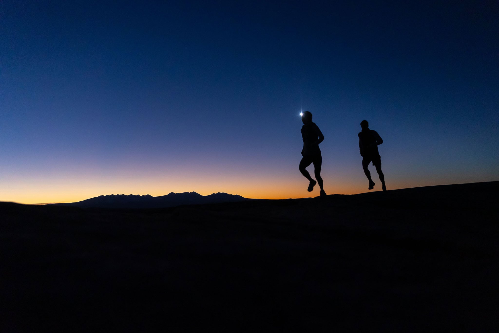 Two people jog along a trail illuminated by a headlamp.