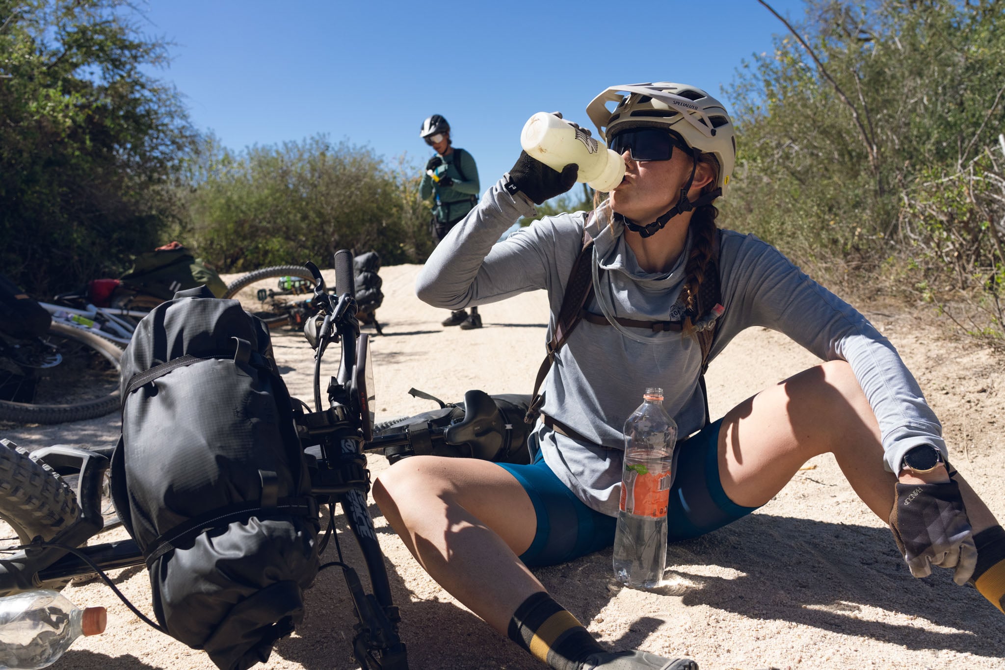 A person sits next to their bike drinking water.