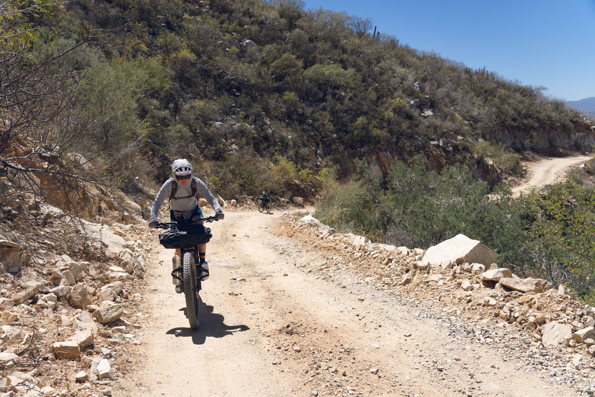 Two people bike fully loaded bicycles up a dusty rocky road.