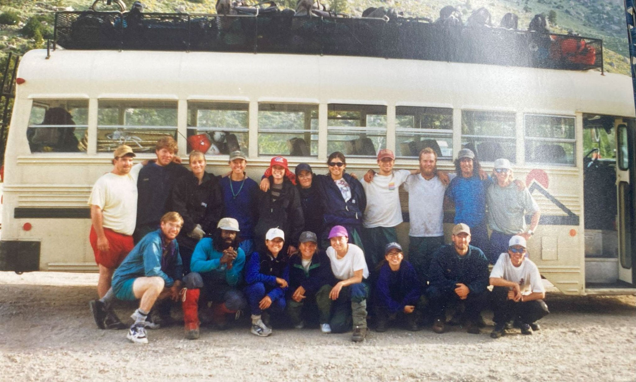 A group of people pose in front of a bus loaded with gear.