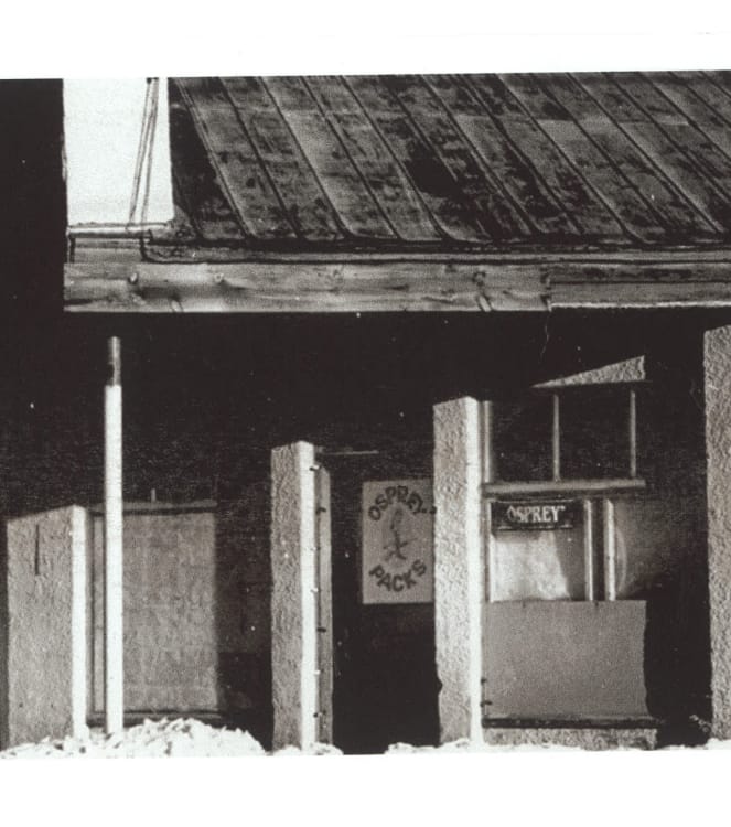 Black and white photo of a stucco building exterior. A sign on the front door says &ldquo;Osprey Packs,&rdquo; and a sign in a window says &ldquo;Osprey.&rdquo;