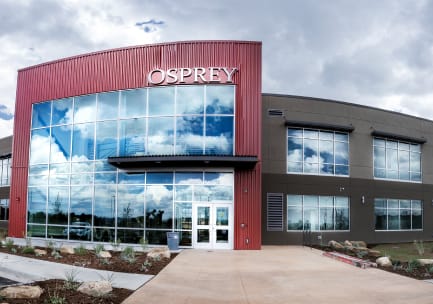 A fisheye photo of a large, charcoal and red rectangular office building with a panel of windows on the main fa&ccedil;ade and stainless steel lettering that says, &ldquo;OSPREY&rdquo;