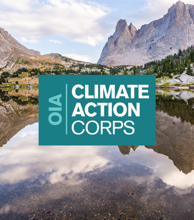 The teal and white OIA Climate Action Corps logo over a photo of a granite and forested mountain area with a glassy, reflective alpine lake and a blue sky.