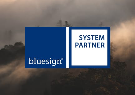 The dark blue and white bluesign SYSTEM PARTNER logo over a photo of a misty, treed mountain.